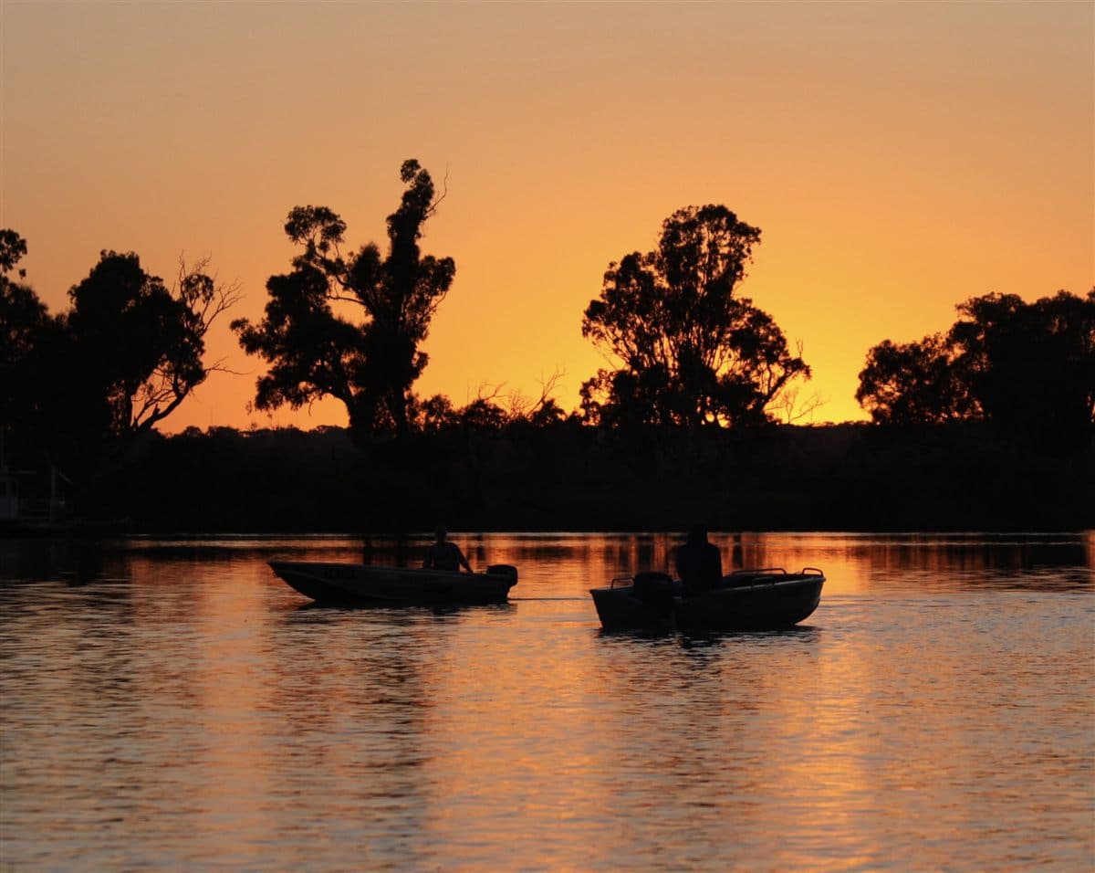 Two tinnies on the still river at sunset with river gums behind