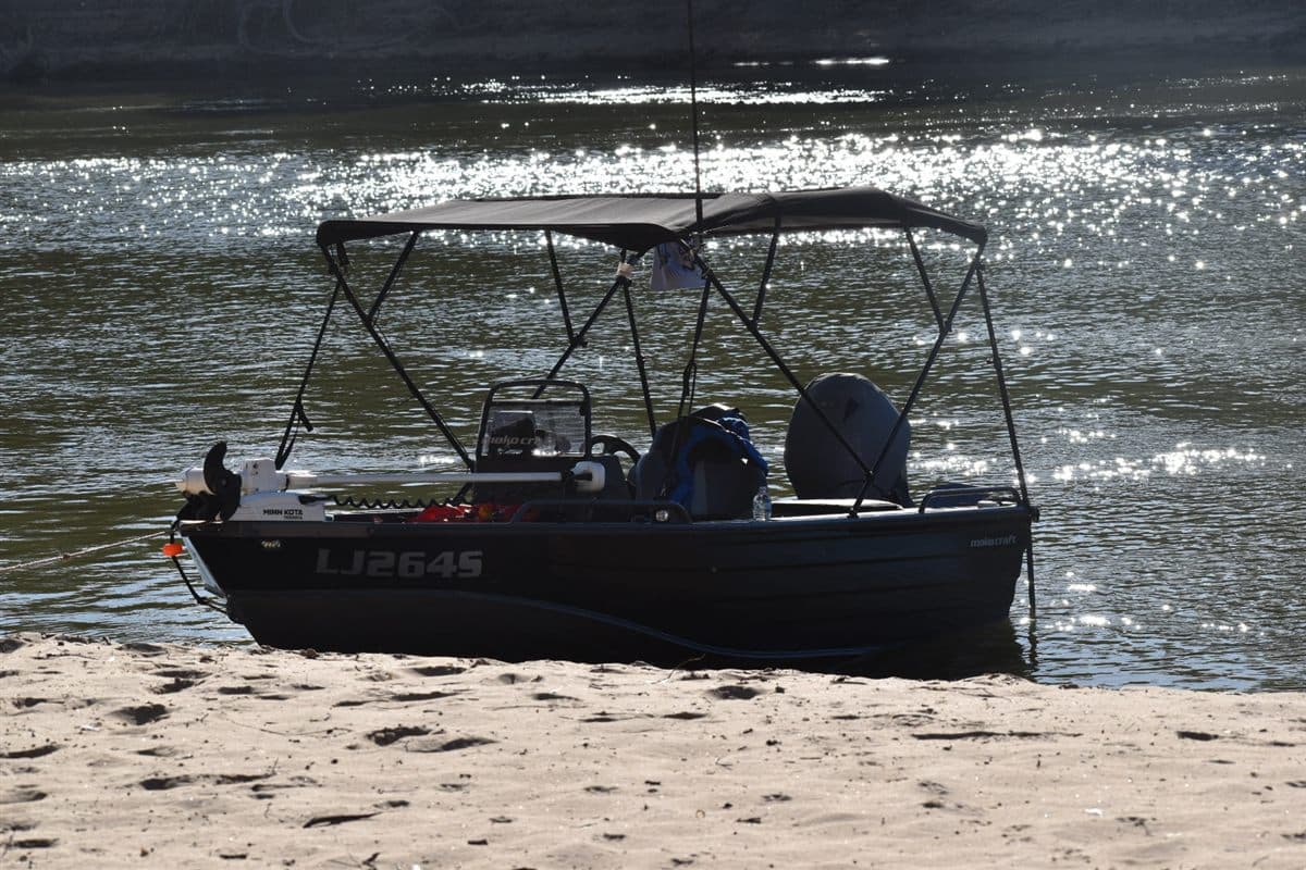 A tinny with an electric trolling motor beached on a sandy riverbank