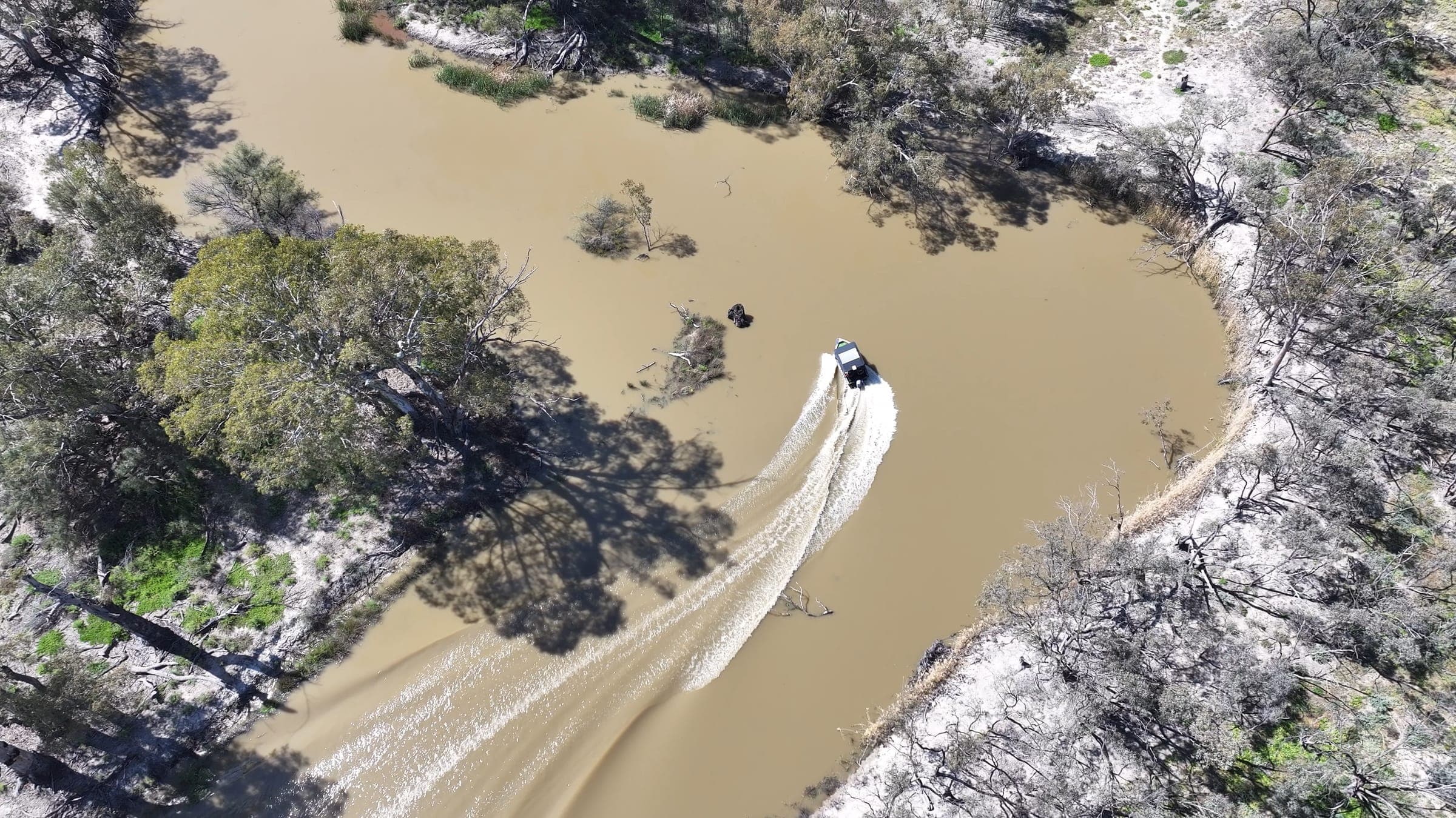 Aerial view of a tinny leaving a wake through a winding backwater creek