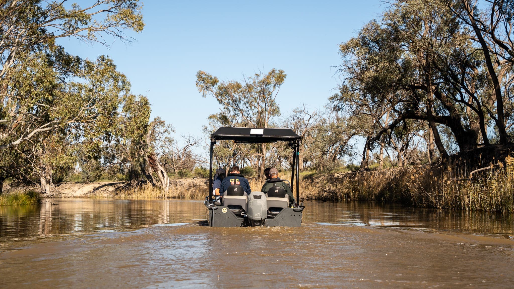 Guests in the tour tinny drifting quietly down a tranquil creek surrounded by river red gums