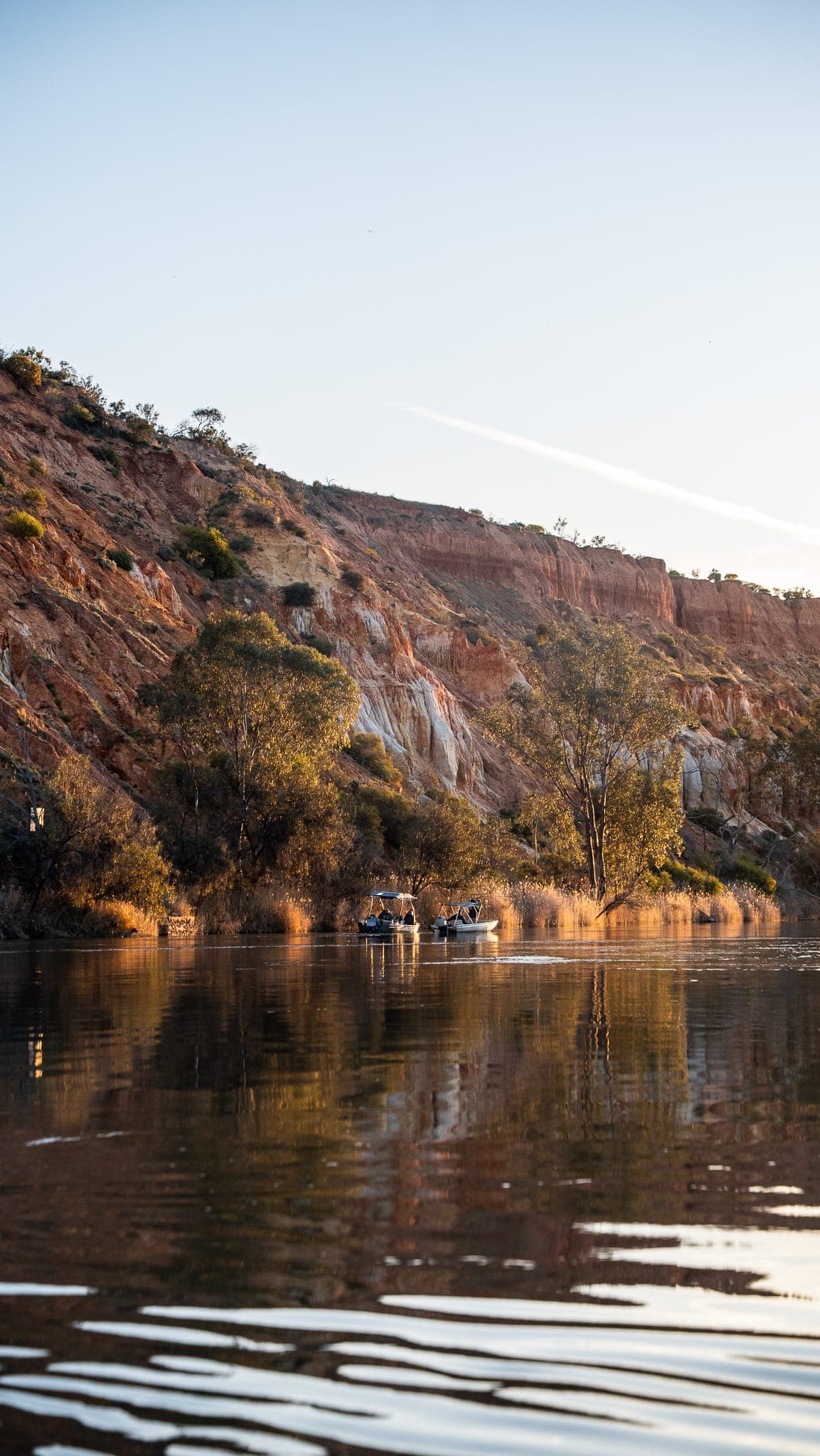 Two tinnies on the Murray River beneath glowing red cliffs in late-afternoon light