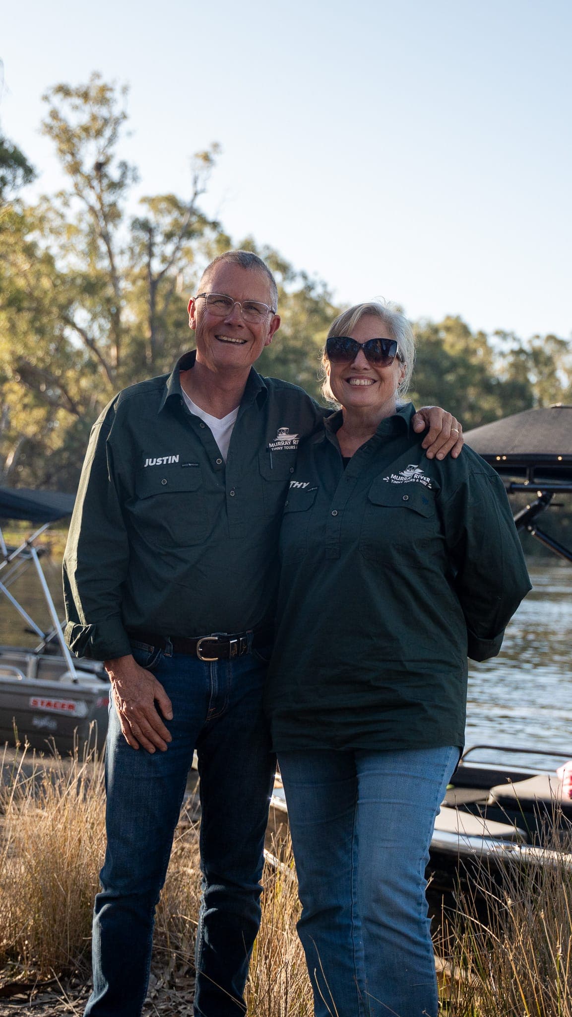 Justin and Kathy smiling on the riverbank in Murray River Tinny Tours shirts