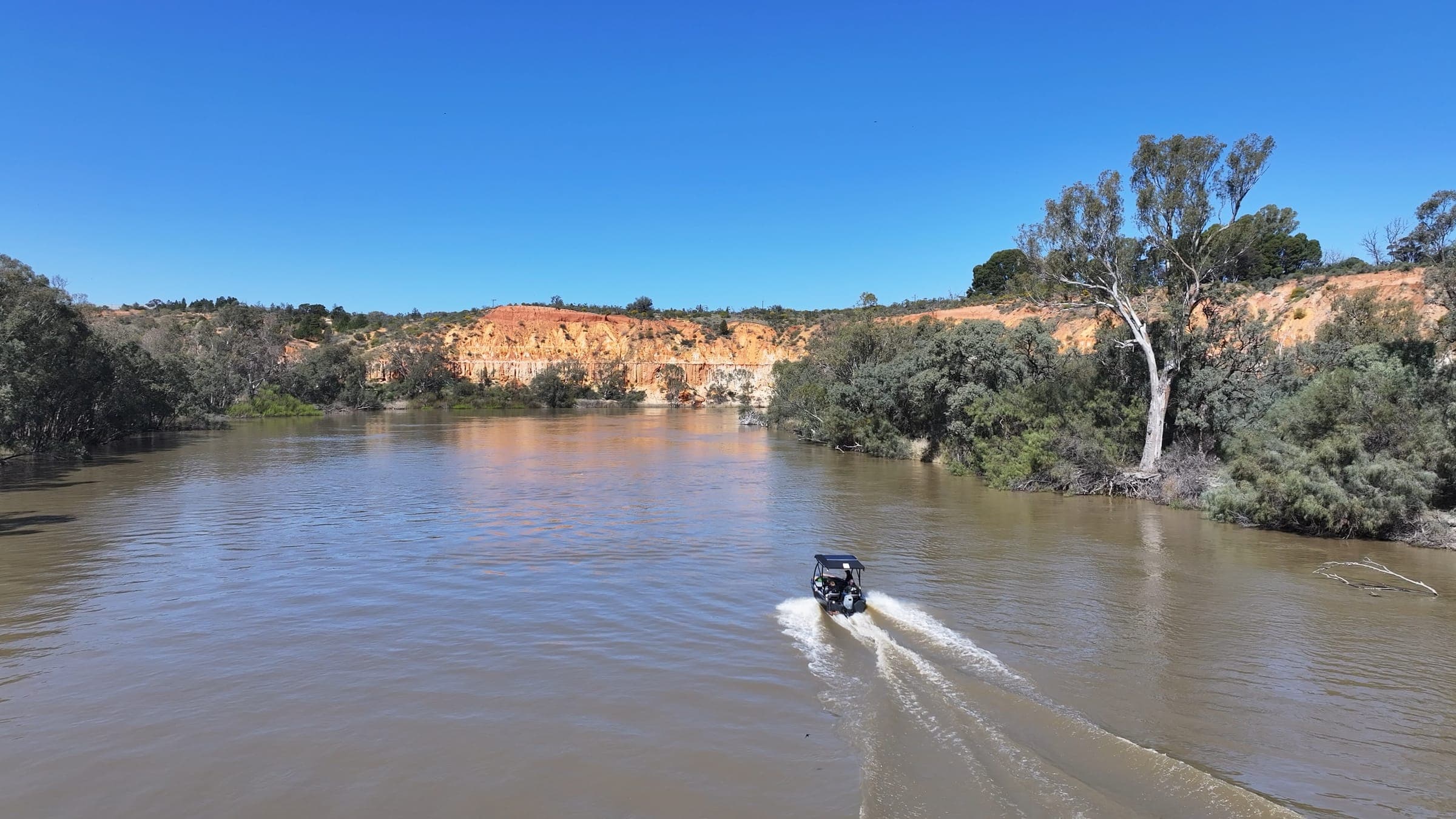 Tour tinny cruising down the Murray River towards sunlit orange cliffs