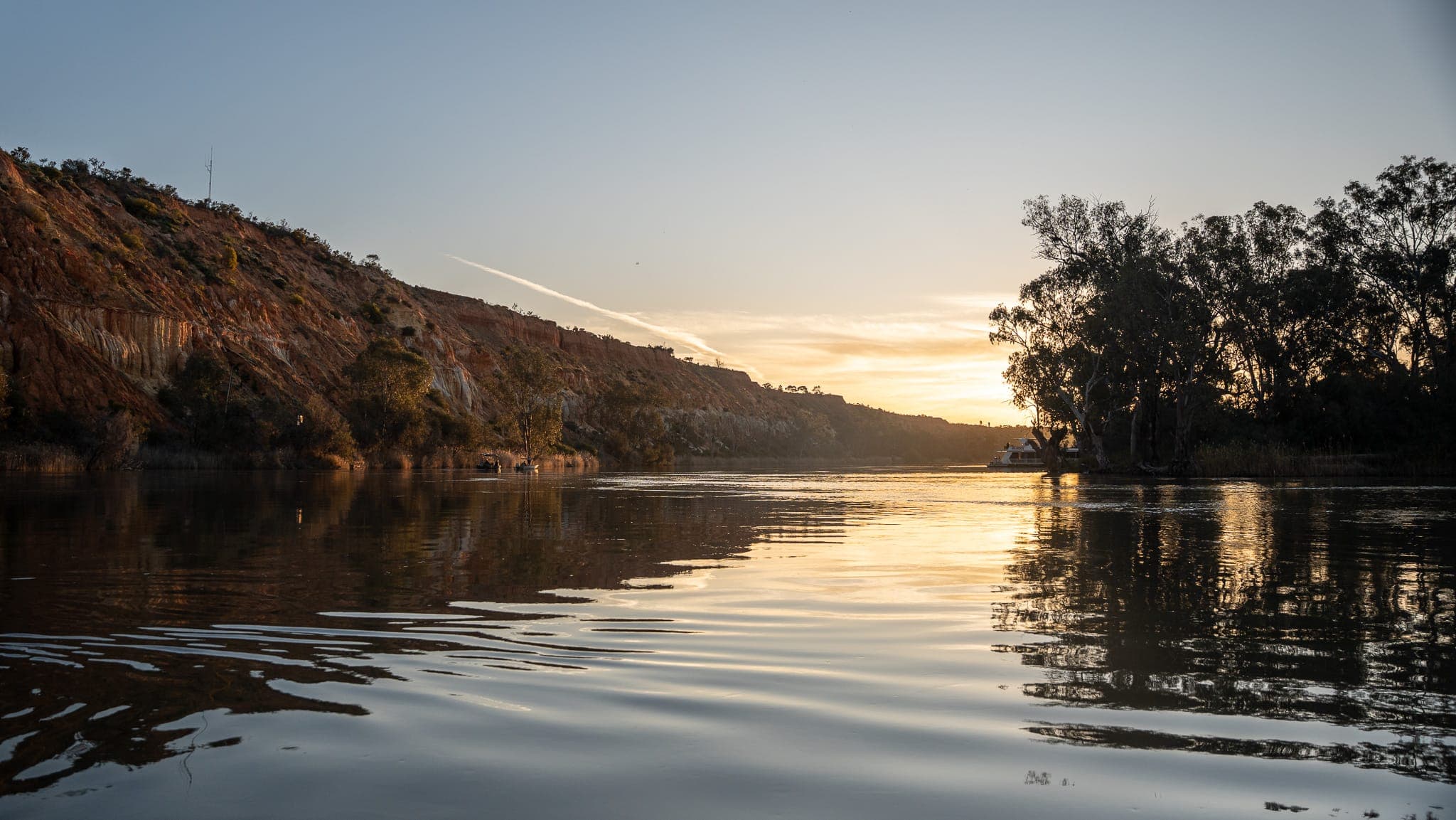 Evening sun setting over the Murray River reflecting off the water beside rugged ochre cliffs