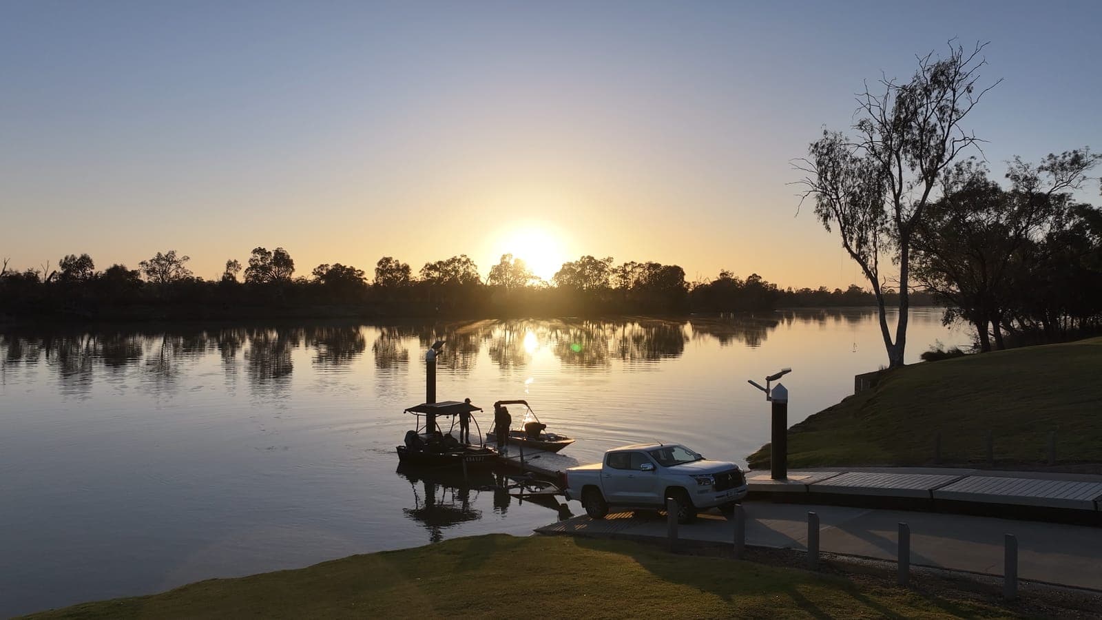 Tinnies tied up at a boat ramp pontoon as the sun sits low over the Murray