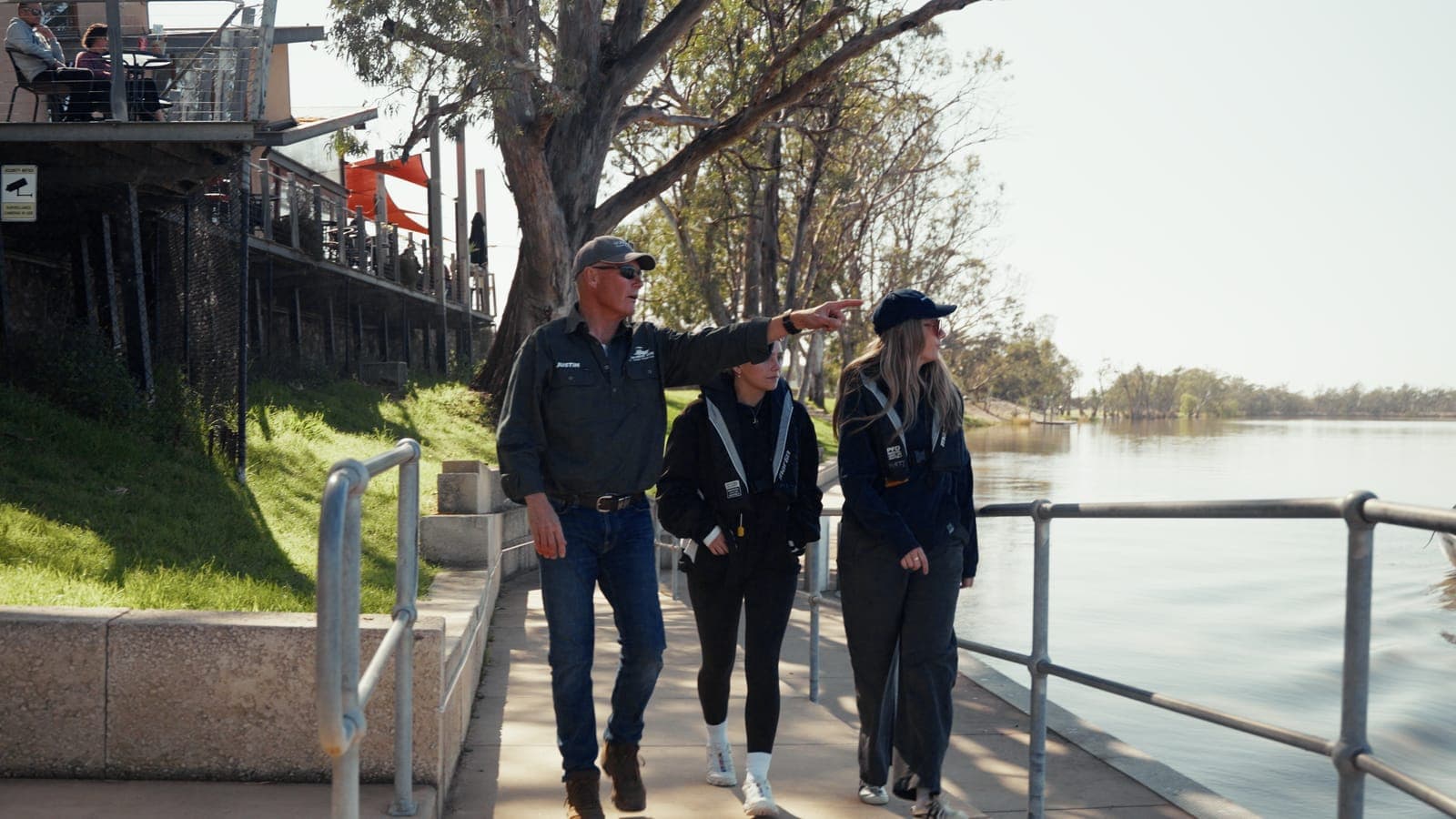 Justin pointing out the river to two guests in lifejackets on a riverfront walkway